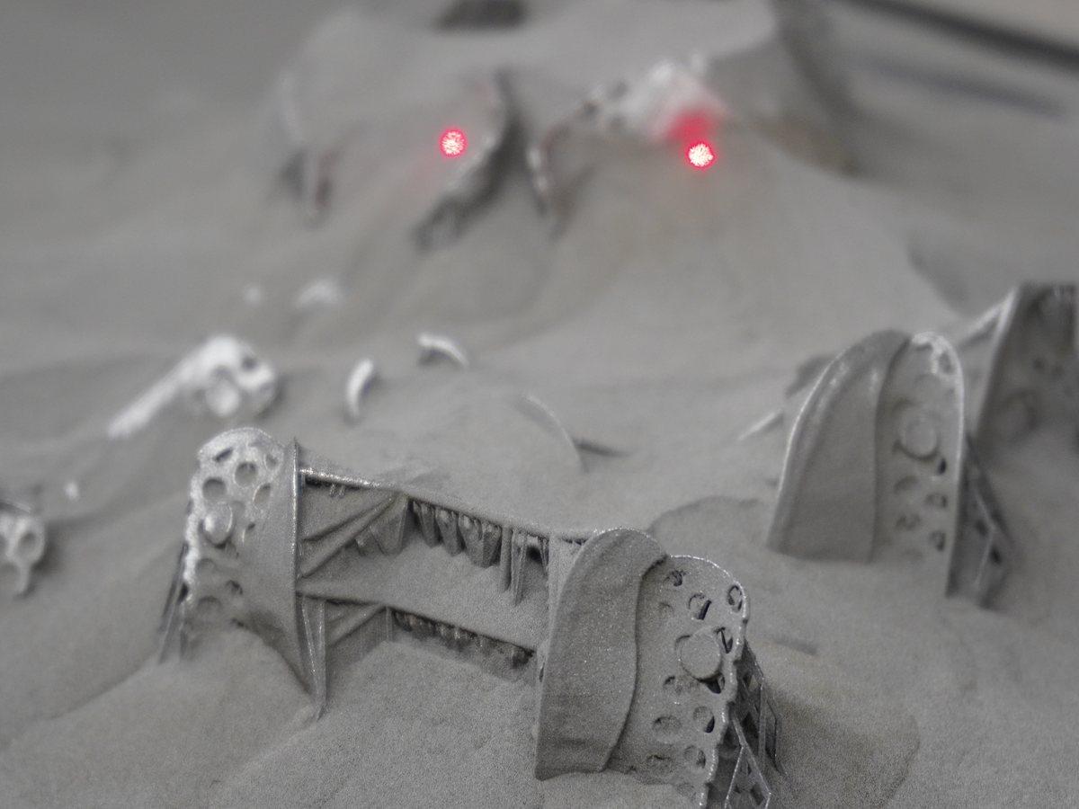 Printed frameworks rising out of the metal powder bed, the build laser's red spots still visible