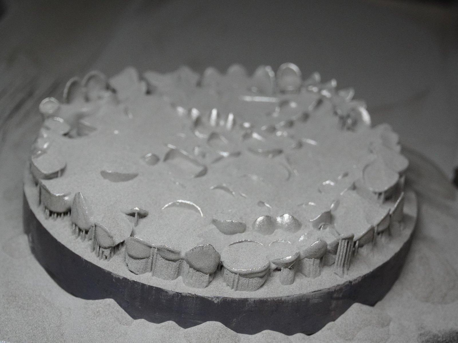 A build plate of crowns half-buried in metal powder after a run